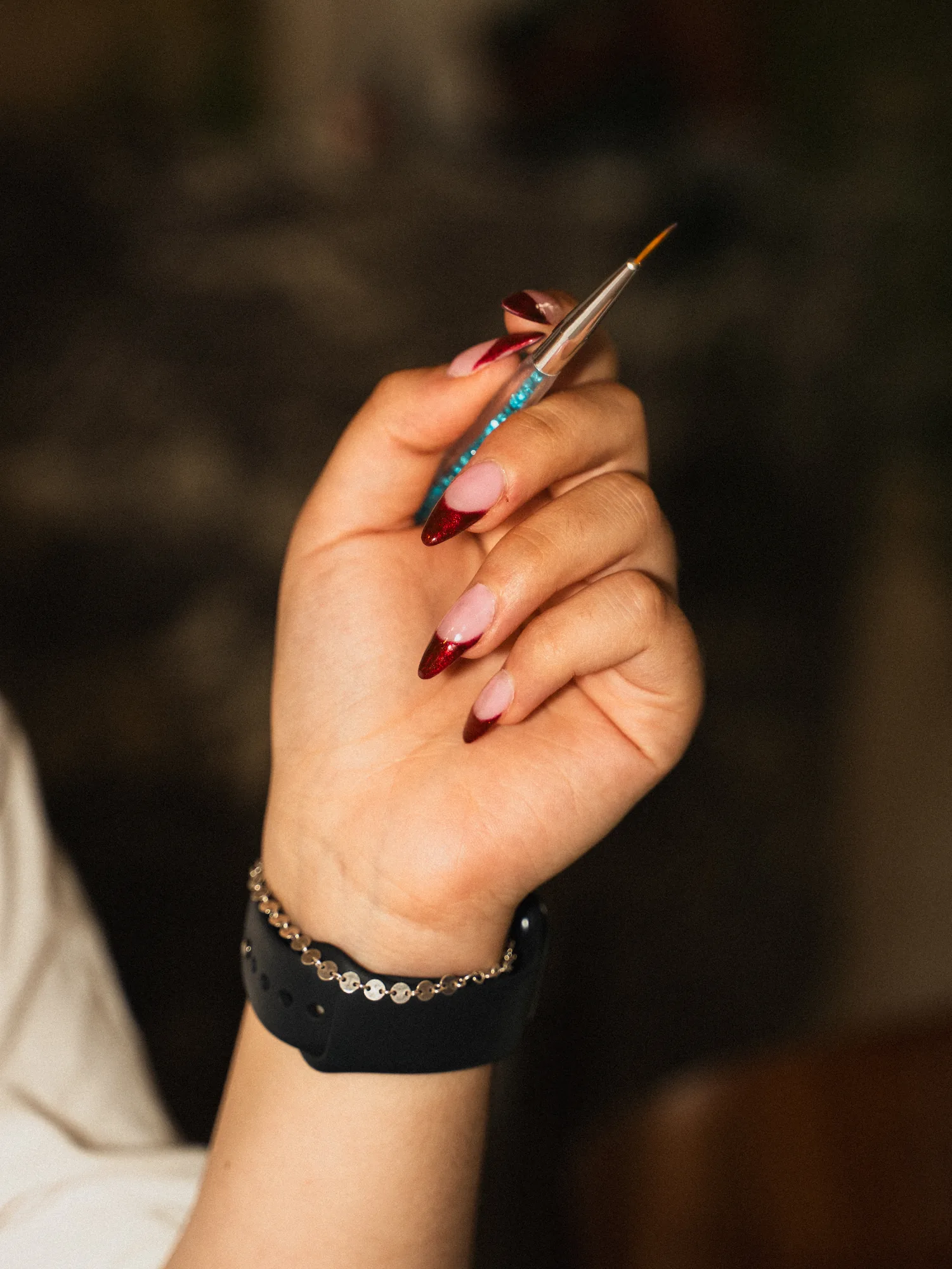 Détail d'une manucure french pailletée rouge, pinceau de nail art en main